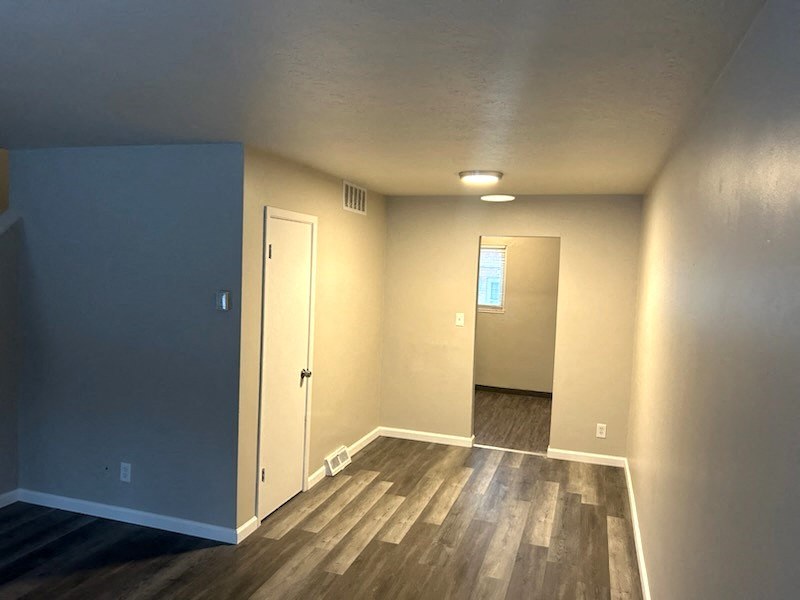 an empty living room with wood floors and a door to a hallway
